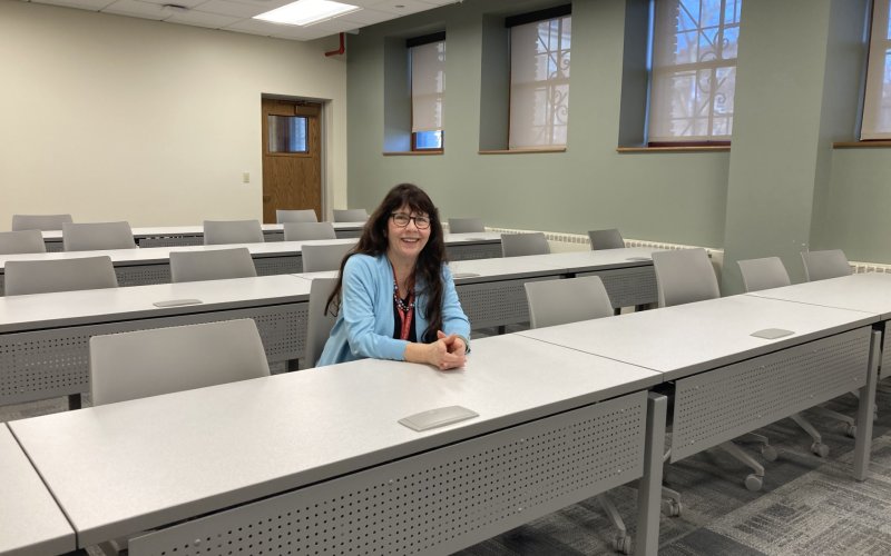 A smiling Mary Bayham sits in a row of seats inside a classroom. 