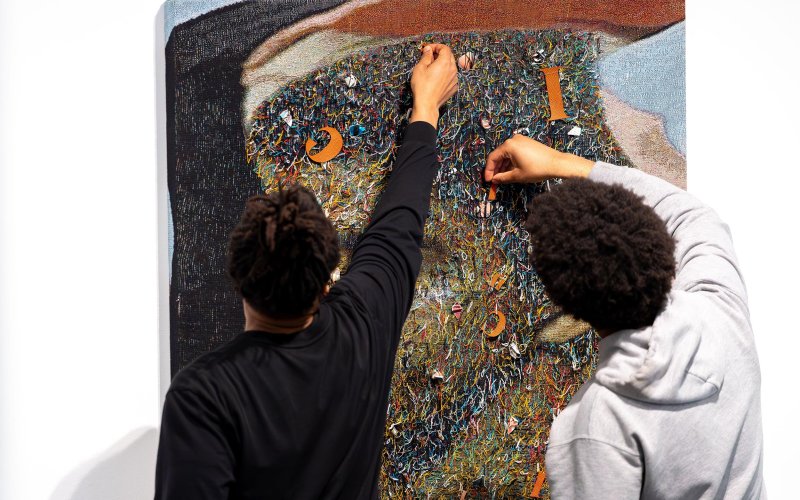 Two young African American students work with a fabric art piece in the University Art Museum by artist Noel W Anderson.