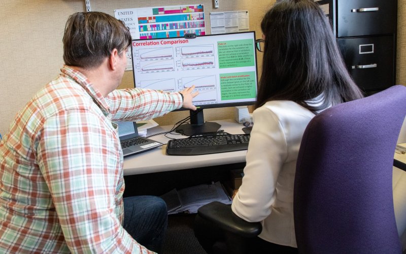 Professor seated next to student points to computer screen in front of them on a desk. 