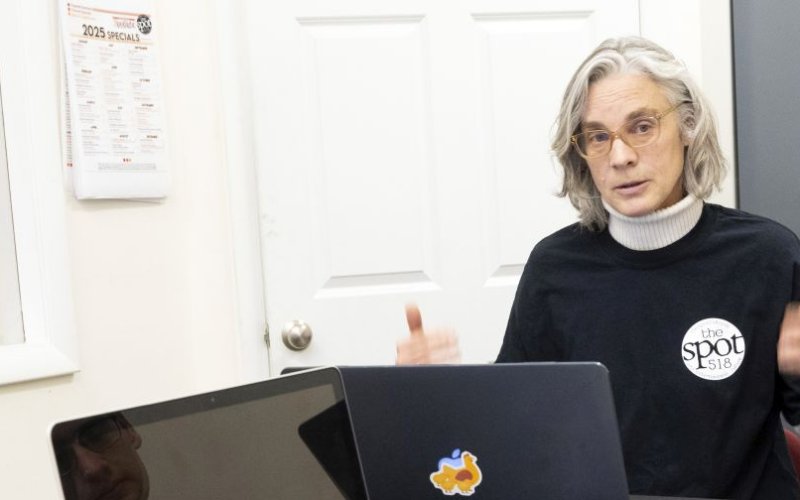 A women in glasses and a dark sweater with the words "the SPOT 518" in a white circle.