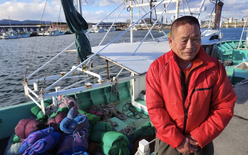 Haruo Ono a weathered man from Japan stands in front of his fishing trawler at Shinchi harbor, Fukushima.