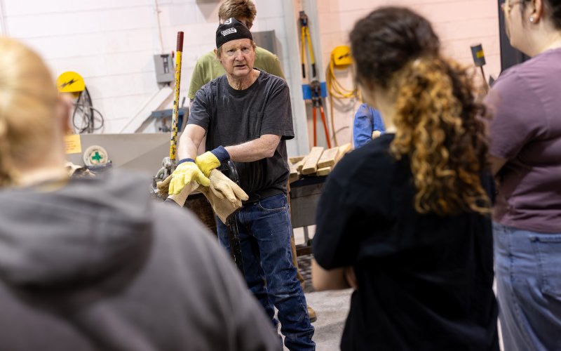 Roger Bisbing, instructional support technician in sculpture speaks with students inside the Boor Sculpture studio during a metal pour. ( Photo by Patrick Dodson)