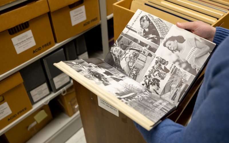 Photo of person holding yearbook opened to a page of photos in the stacks