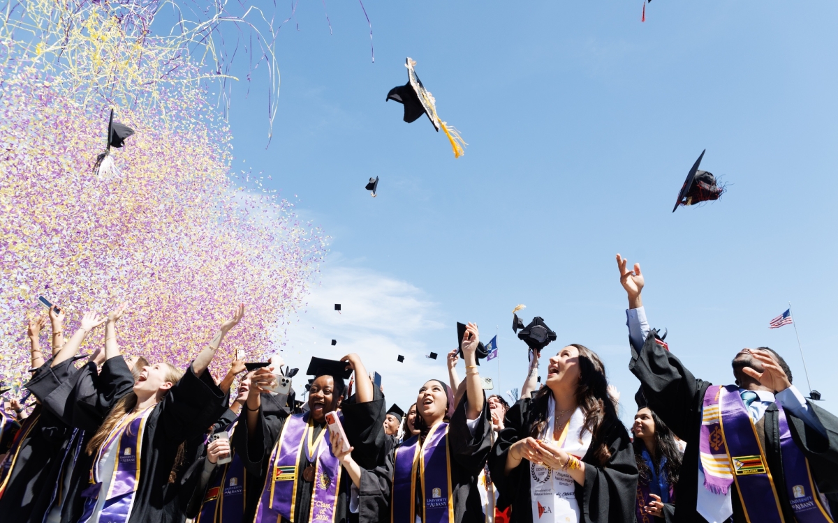 Graduates are showered with confetti while they throw their caps in the air in celebration.
