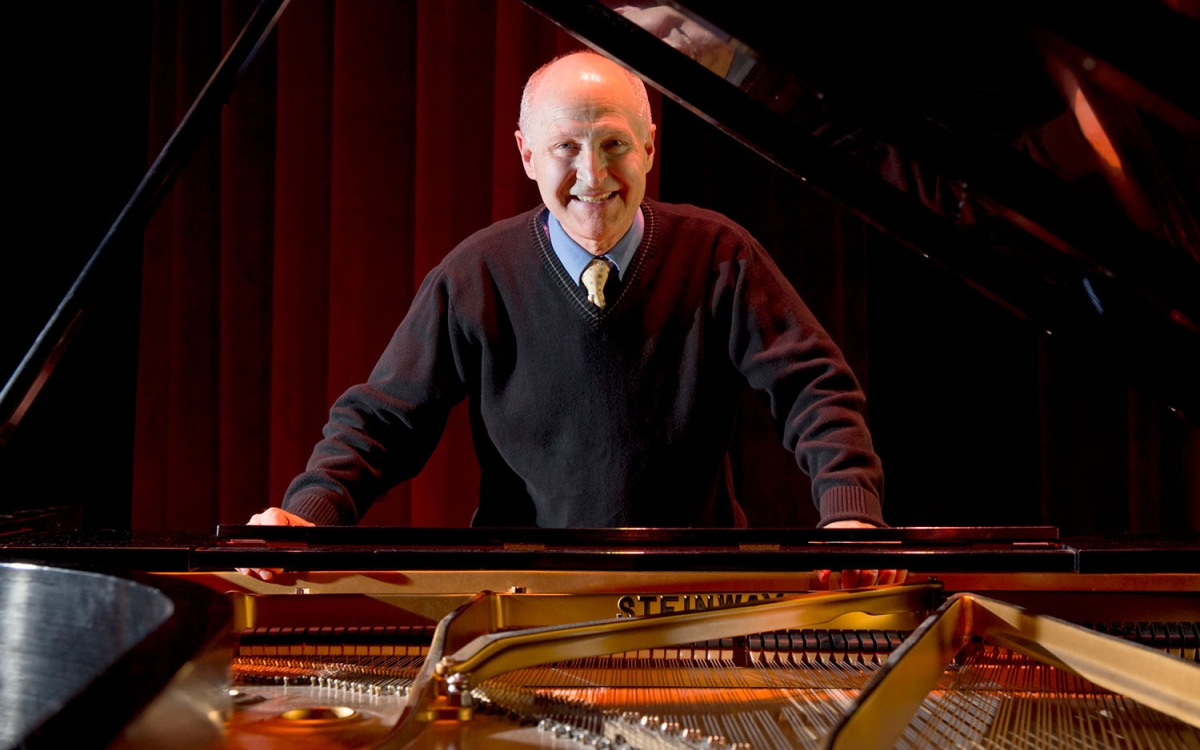 musician stands smiling behind keyboard of grand piano
