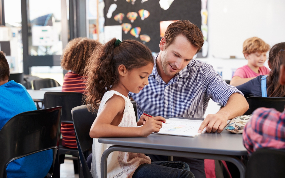 A teacher showing something on a piece of paper to a young child.