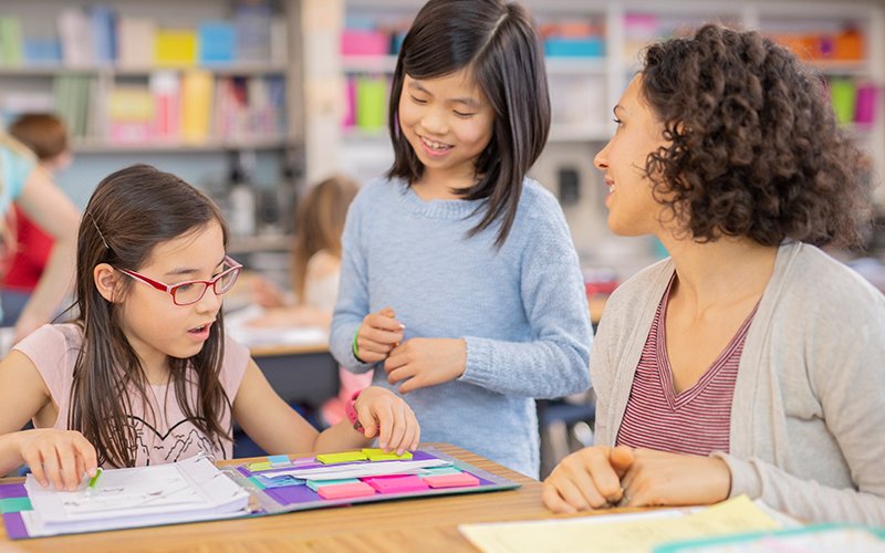 An image of a teacher talking to two young students.  