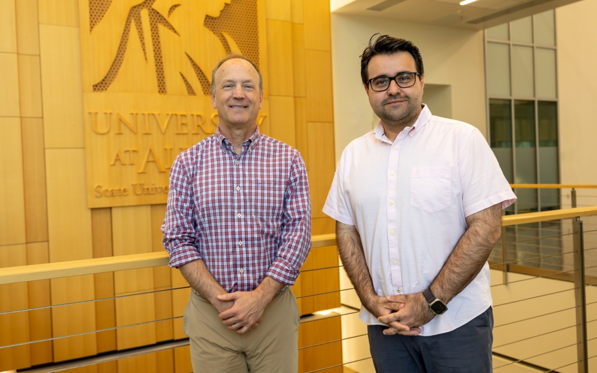 Andy Berglund and Abdullah Canbaz stand in front of a Minerva wood panel at ETEC.