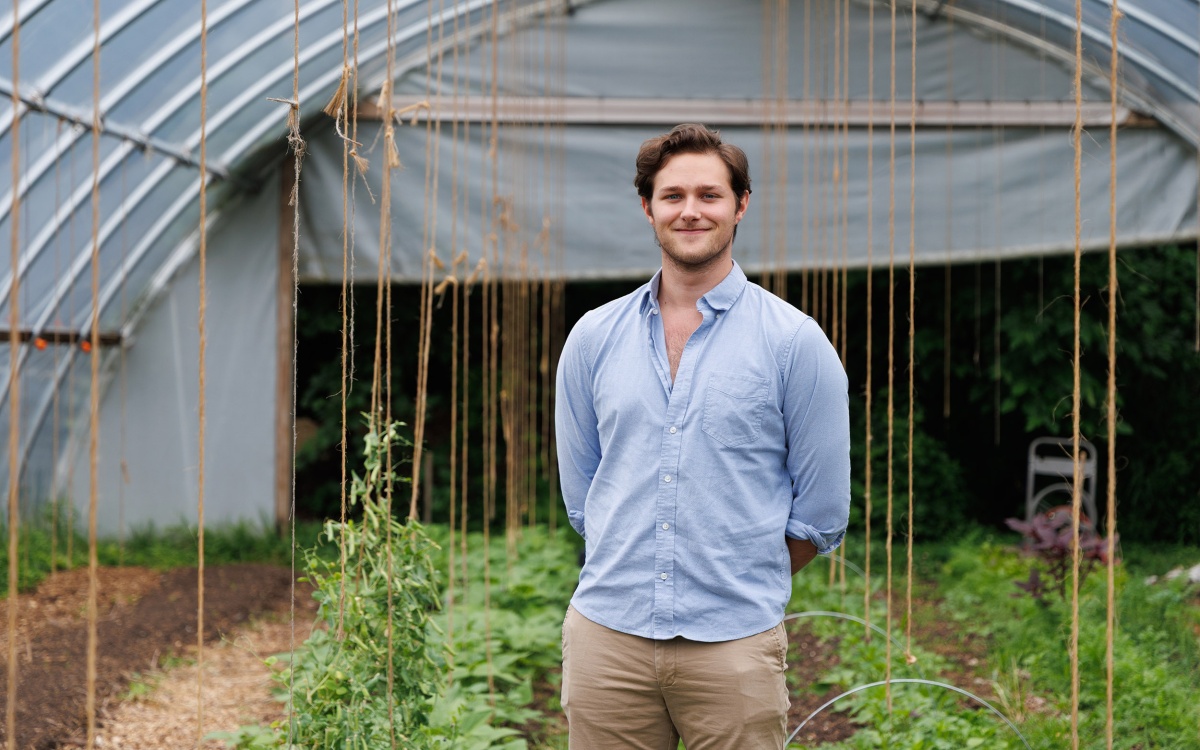 A man in a blue collared shirt stands in a greenhouse in front of rows of small plants.
