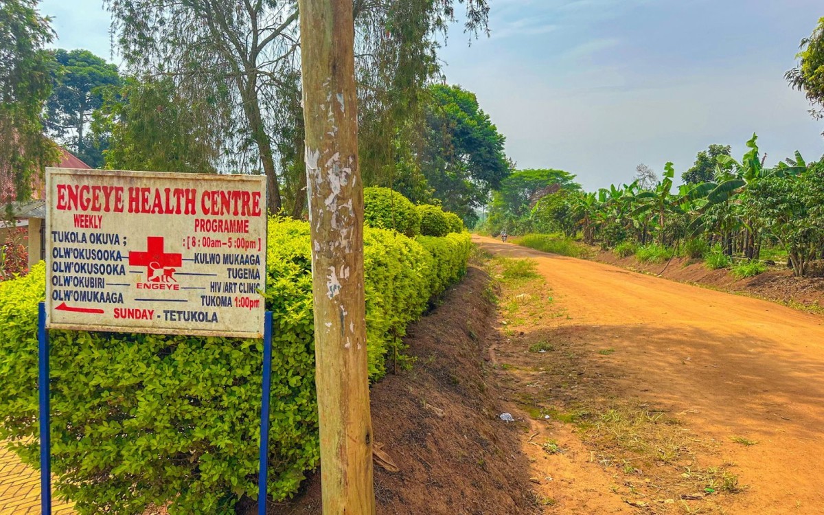 A dirt road and a sign that says "Engeye Health Centre" with a medical red cross on it.