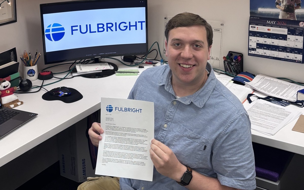 Chris Gilberti holds up a Fulbright offer in front of a computer screen.