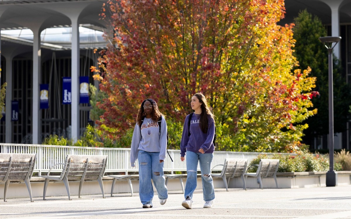 Two students walking around UAlbany's main campus during the fall.