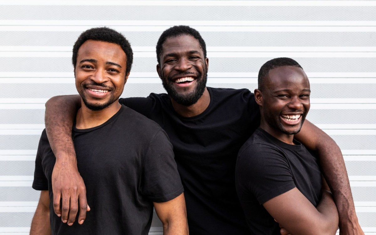 Three men smiling, the middle man has his arms around the other men's shoulders.