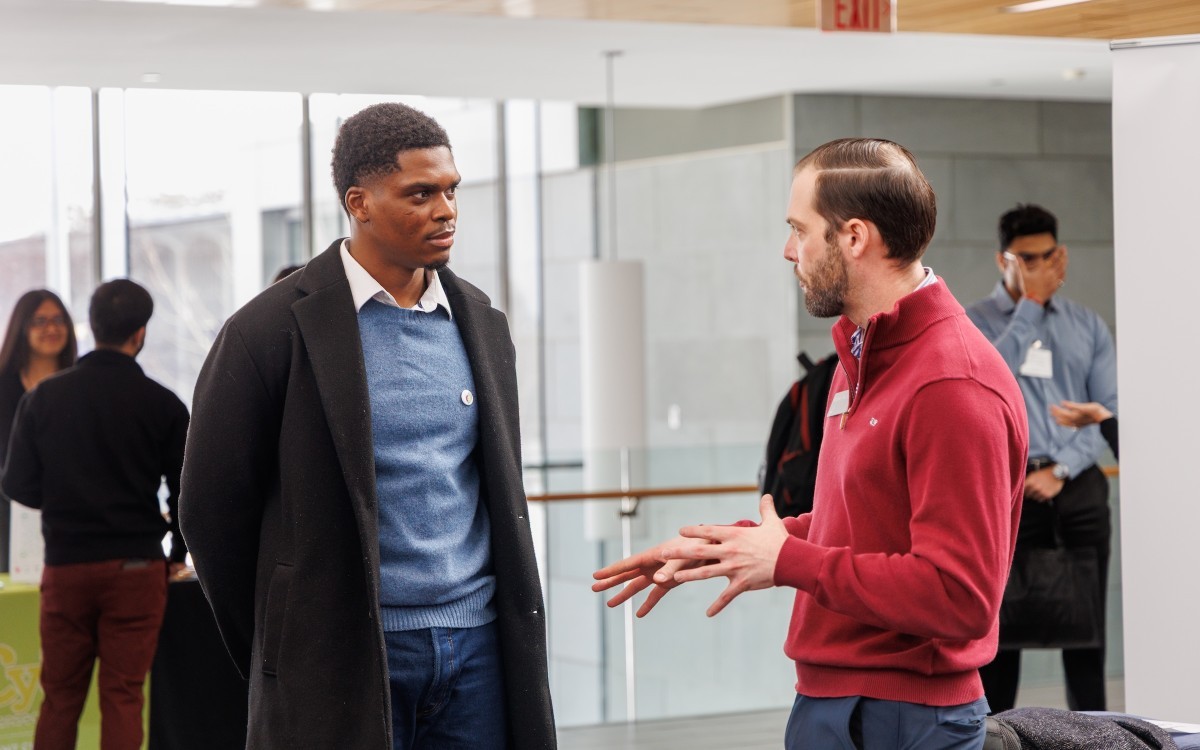 Young man in a long coat looks at older man as he talks.  