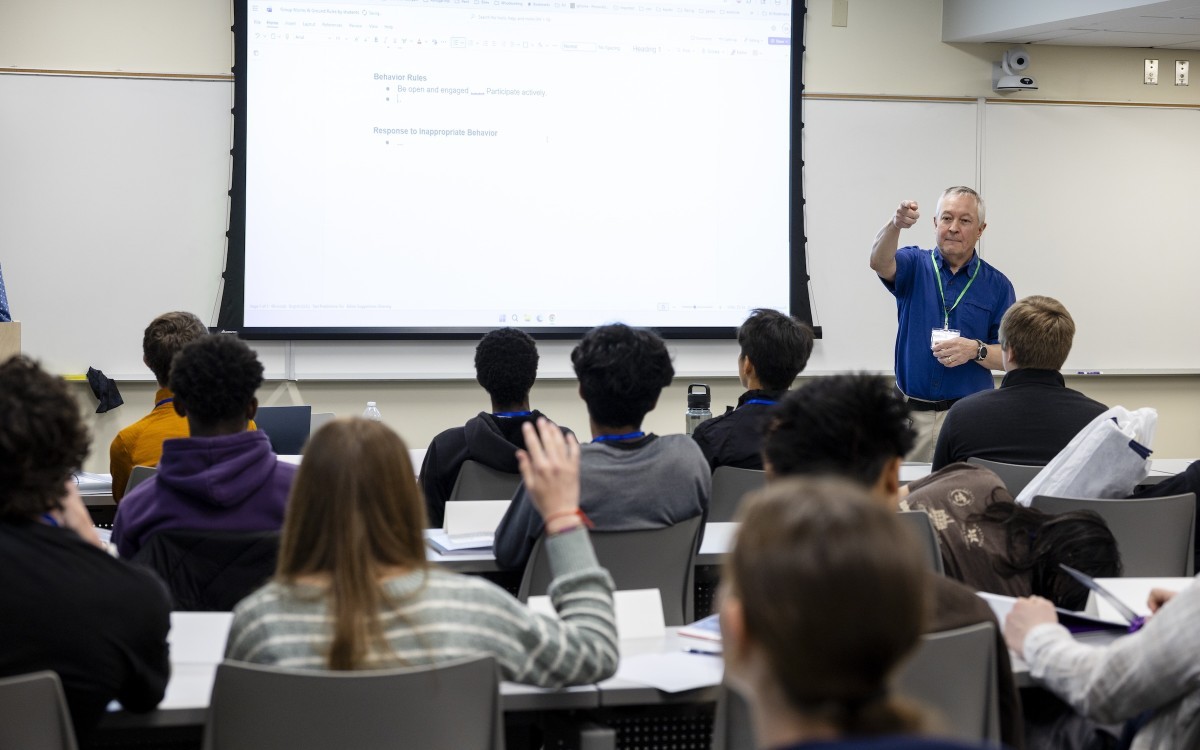 Instructor at the front of a classroom points to student raising her hand. 