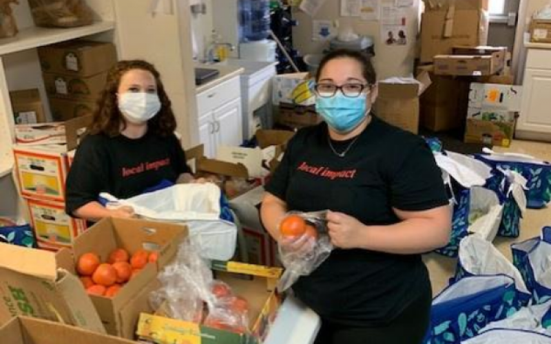 Elizabeth and a coworker bag oranges into plastic bags. They are wearing face masks.