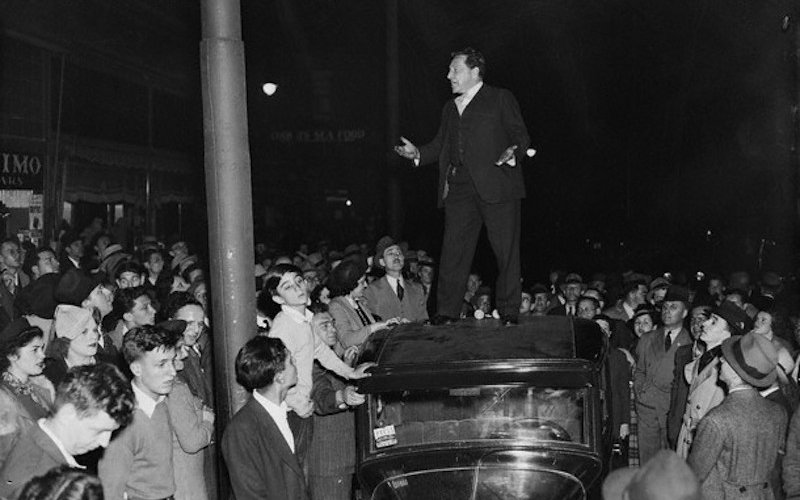 Man standing on car surrounded by crowd