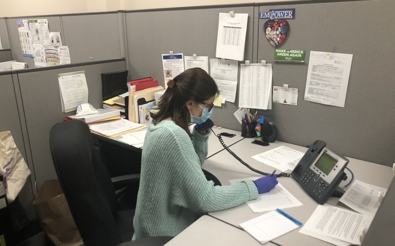 Makensy Jabbour sits at a desk wearing a mask and gloves. She is on the phone as a part of her COVID-19 response work with the local health department.