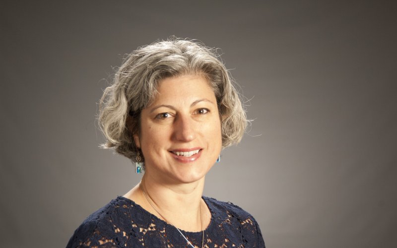 Dr. Janine Jurkowski smiles at the camera, standing against a grey backdrop.