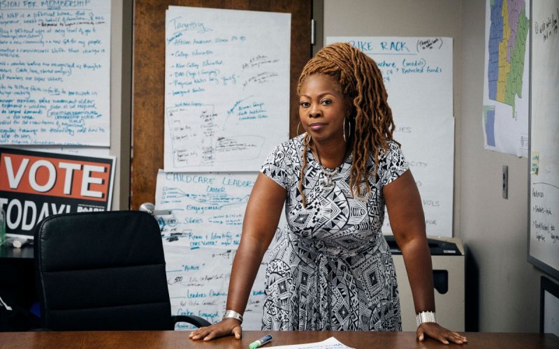 LaTosha Brown stands, leaning on her desk, surrounded by whiteboards covered in writing