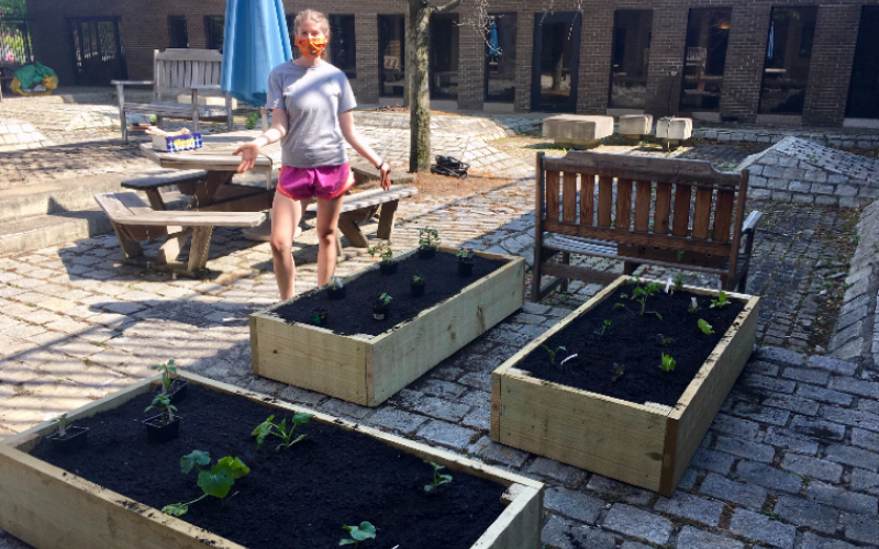 Leanna stands next to three wooden plant beds she has just created. They are outside on a brick patio, filled with dirt.