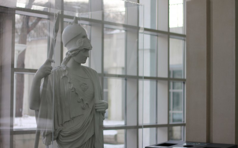 A statue of Minerva stands in the Science Library atrium. Glass windows are behind her.