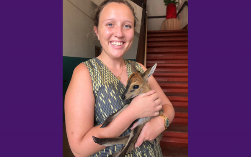 Alyssa smiles at the camera. She is indoors holding a baby kangaroo.
