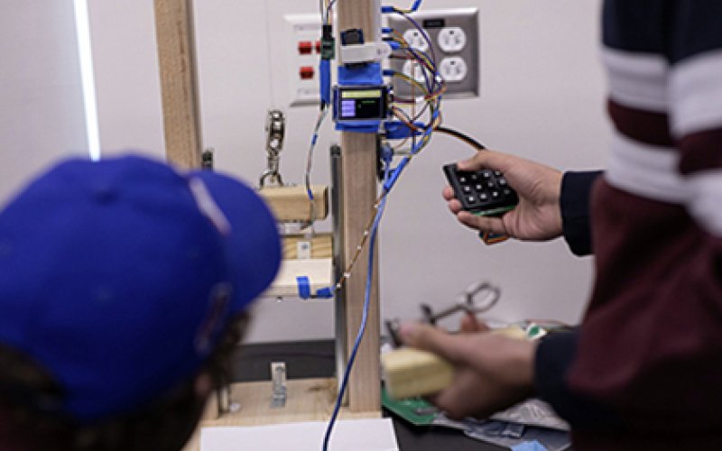 A student pushes buttons on a wooden device indoors.
