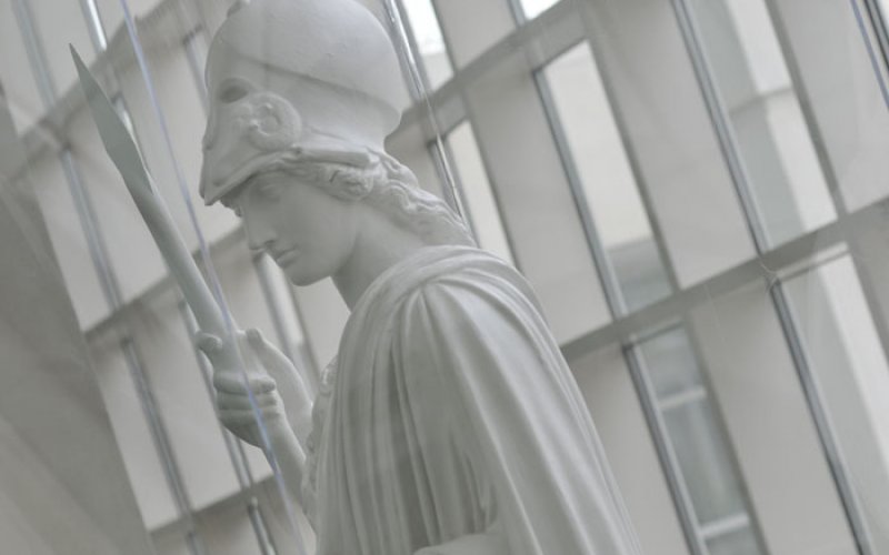 A white statue of Minerva stands in the Science Library atrium. Glass windows are behind her.