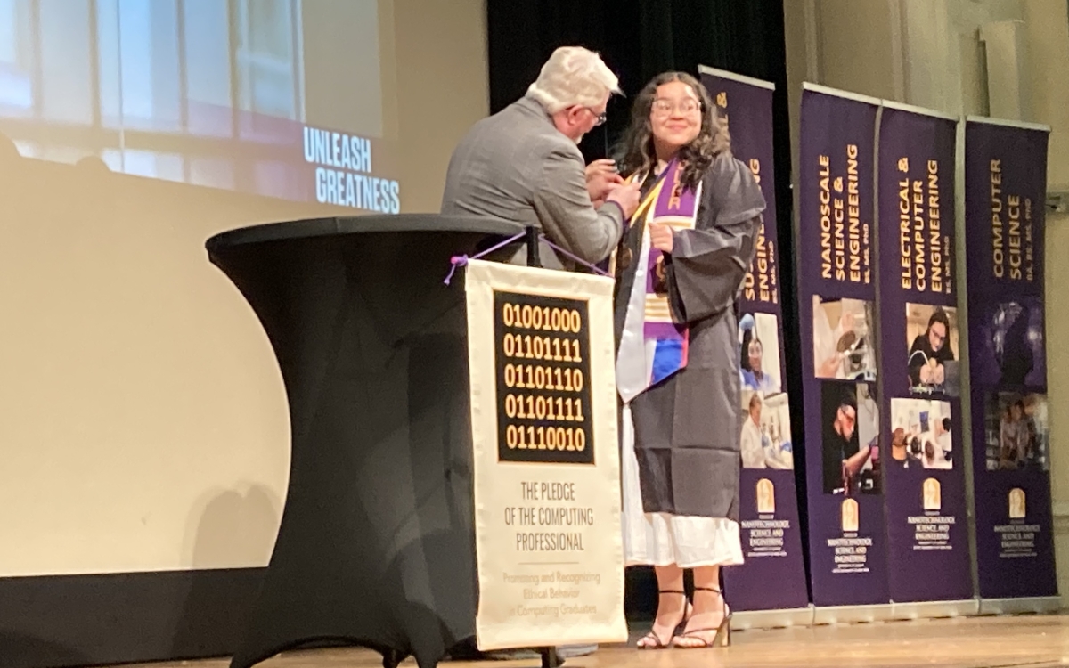 Computer science chair attaches pin to robe of new graduate.