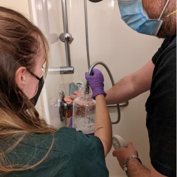 Noelle Horth is holding a jug up to a shower to sample it for Legionella.