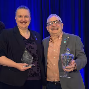 Smiling Michele Grimm and David Kaplan holding awards. 