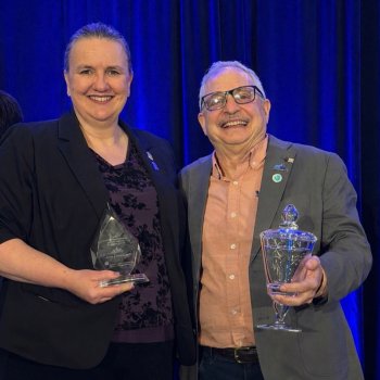 Smiling Michele Grimm and David Kaplan holding awards. 