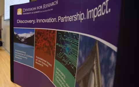 A curved, purple sign with the heading Division of Research displays images and graphics depicting different fields of study