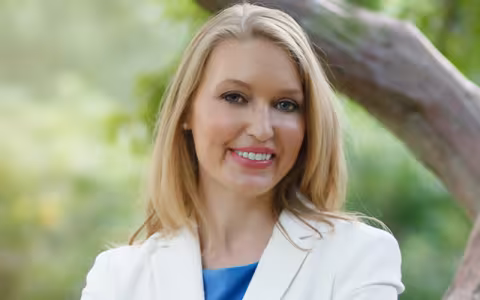 Kelly Wissman in front of a large tree branch and green foliage
