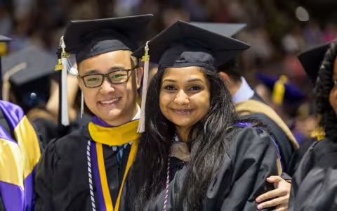 Students dressed in academic regalia take a photo at SEFCU Arena during graduation.