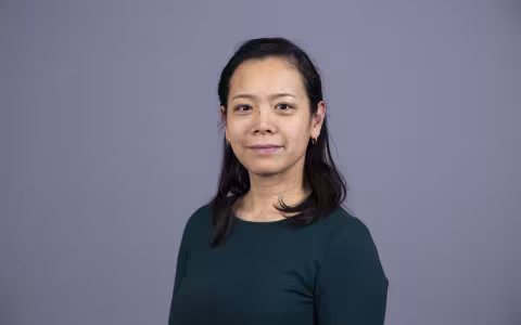 Tomoko Udo stands against a grey background and smiles at the camera.