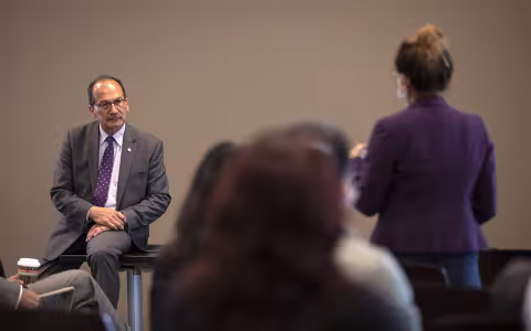 President Rodríguez, seated, listens to a woman ask a question from the audience