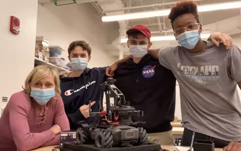Marcie Fraser and three students in the EPICH program stand in front of a robot inside CEHC's makerspace at ETEC. 