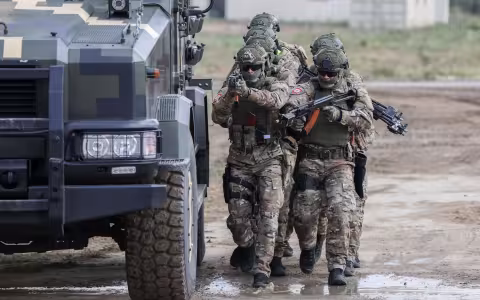 Ukraine military members armed with guns walk next to a transport vehicle on a muddy road during training in 2019.