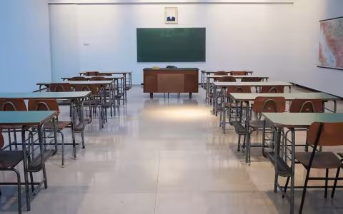 Ana empty classroom with two rows of student desks and chairs and a teacher's desk in front