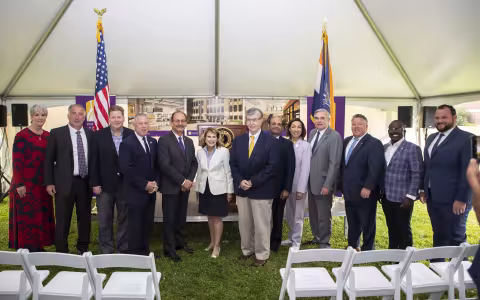 A group of people stand posed for a photo inside of a tent with the U.S. and NYS flags behind them