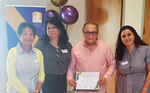 Four smiling people stand in front of a UAlbany banner. Man in center holds a certificate. 