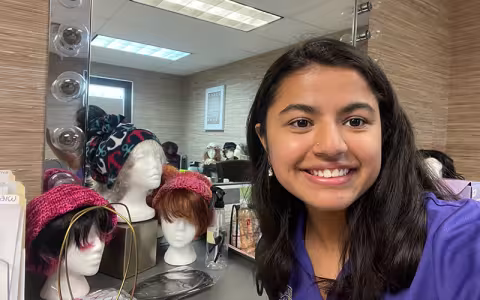 Labika takes a selfie in front of a mirror and a display of wigs.