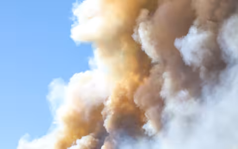 White and brown smoke covers a blue sky.