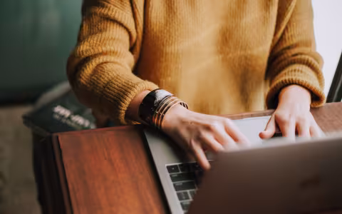 A woman works on her laptop from home office with only her hands visible typing.