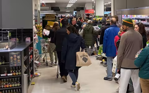 People stand in line holding their goods, waiting to check out of a grocery store.