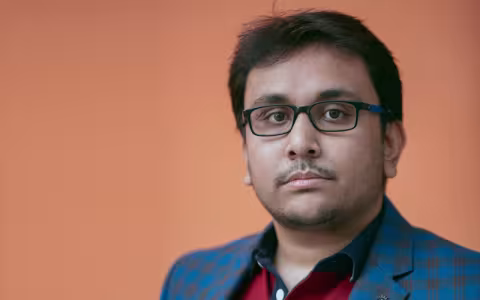 Jayanta Talukder stands in front of a soft orange background