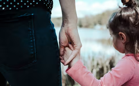 A woman holds a small child's hand.