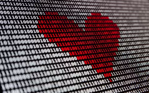 Image is of binary code - the digits one and zero. The numerals are white and the background is black. In the middle, the digits are rendered in red, forming form a heart shape. 